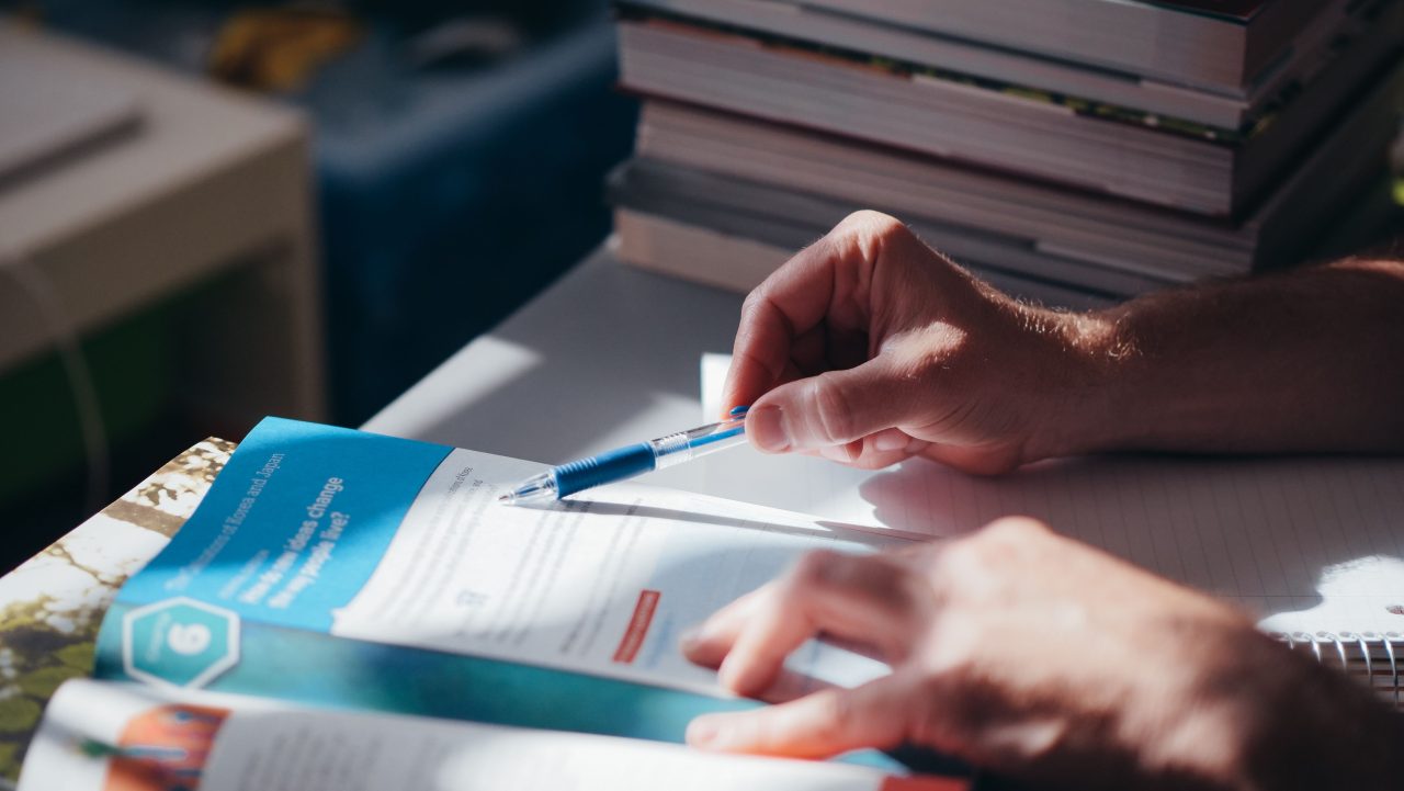 Close-up of hands writing at a desk with an open notebook and pen