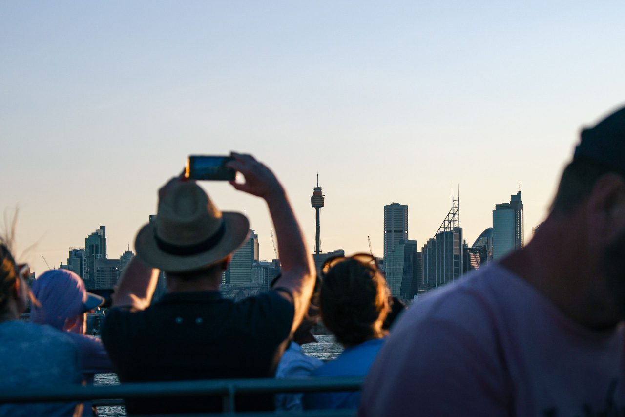 Travellers on a boat photographing a city skyline at sunset.