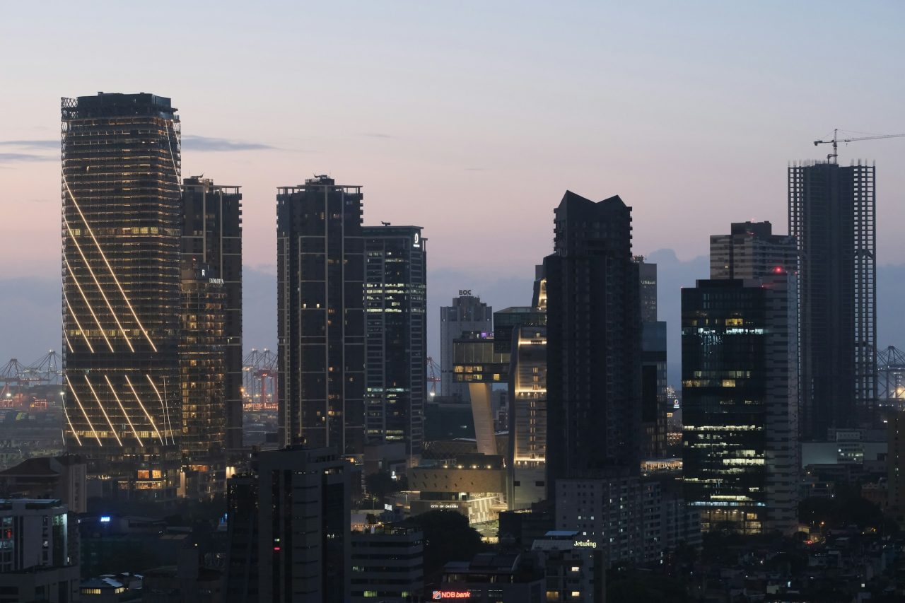 A city skyline of high-rise offices lit at dusk.
